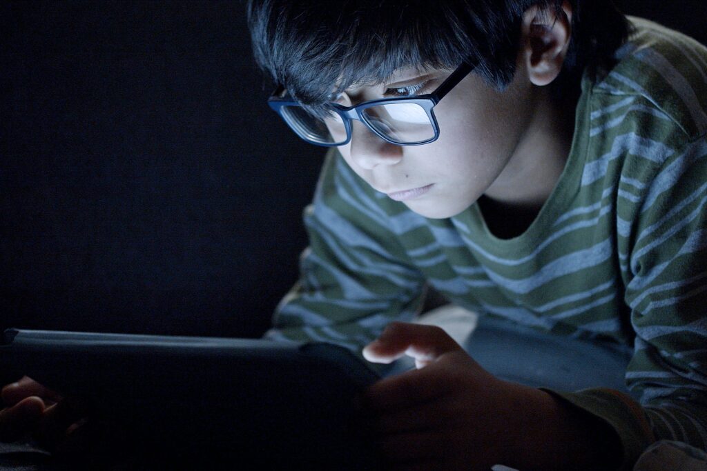 Boy Wearing Eyeglasses Using a Tablet in the Dark Room